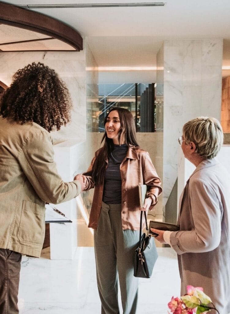 Three female presenting professionals greeting each other in office lobby