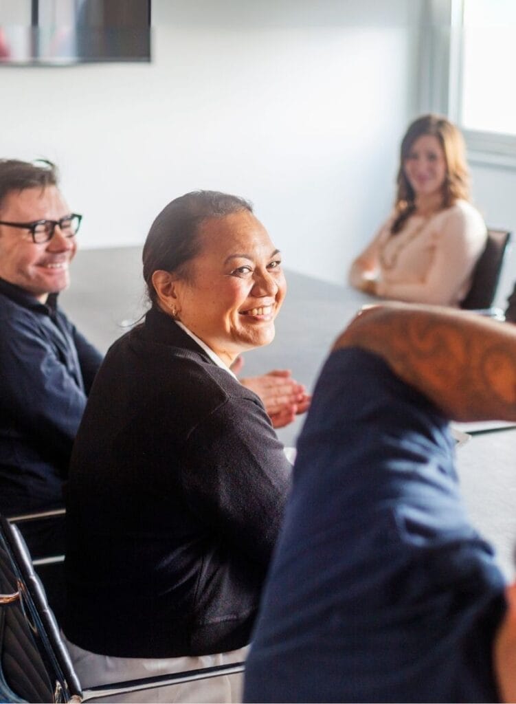 Smiling female-presenting worker at boardroom table surrounded by colleagues